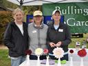 Three women at a Bullington Gardens booth with cut flowers on a table