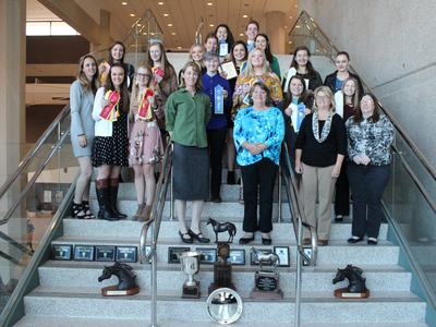 Group of students and adults on staircase holding ribbons; trophies displayed on steps.