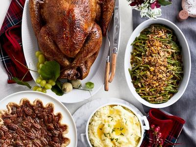 Roasted whole turkey on platter surrounded by pecan pie, mashed potatoes, and green beans