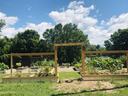 Raised vegetable garden beds behind a wooden arch gate with trees and blue sky