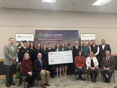 Group of people holding oversized check for $107,000 in front of Farm Credit banner
