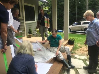 Group of people on a porch reviewing large architectural drawings