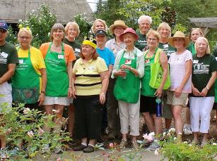 Community gardeners in green aprons standing together in a rose garden