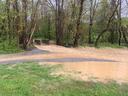 Flooded gravel path with muddy puddle leading to small concrete bridge amid trees