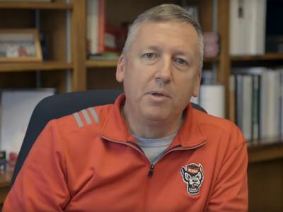 NC State College of Agriculture and Life Sciences Dean Richard Linton sits at his desk in a red NC State shirt while looking at the camera