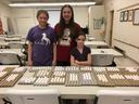 Three girls behind a table of egg cartons filled with white eggs in a community room