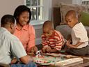 A mom and dad with their two young boys are playing a board game on the table in the living room