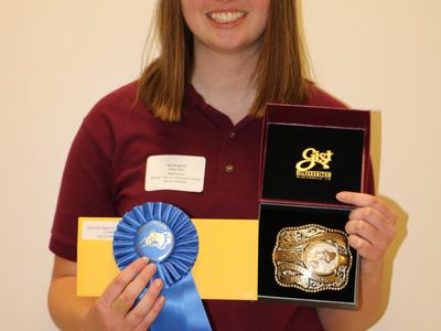 Person holding blue ribbon reading "North Carolina State 4‑H Hippology Contest" and a belt buckle award