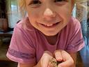 Young girl holding a small chick gently in cupped hands, smiling at camera