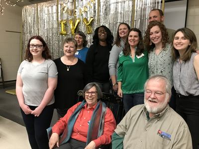 Group of people posing in front of silver fringe backdrop with gold "IVY" balloons