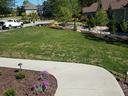 Front yard with sidewalk, green lawn showing patchy brown spots and a planted flowerbed