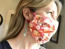Person in side profile wearing pink floral-plaid cloth face mask and dangling turquoise earrings