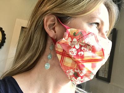 Person in side profile wearing pink floral-plaid cloth face mask and dangling turquoise earrings