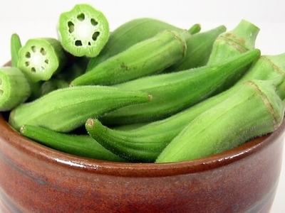 Green okra pods, whole and cross-sectioned, in a brown ceramic bowl