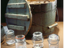 Wooden bucket with lid and handle behind four small glass jars with wire bail closures