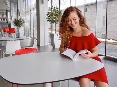 Young woman in red dress sitting at a white table reading a book