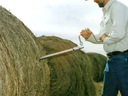 man taking core sample from round bale of hay
