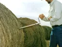 man taking core sample from round bale of hay