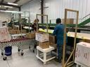 Workers packing green apples into cardboard boxes labeled "Fresh Fruit" on conveyor
