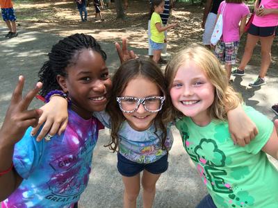 Three girls with arms around each other, one wearing zebra-striped glasses, two showing peace signs
