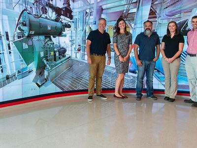 Five people standing in front of a very large screen wall