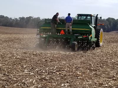 Two men on a John Deere tractor seeder planting across a harvested field