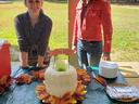 Two women standing behind a table with a white bundt cake decorated with autumn leaves