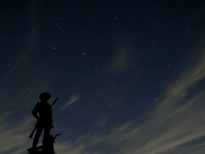 Silhouette of a soldier statue holding a rifle on a pedestal against a starry night sky
