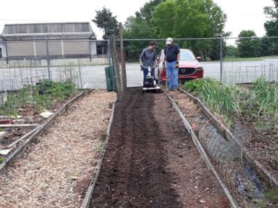 Quina learning to use a new tool in a community garden.