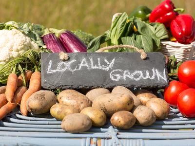 Chalkboard sign "Locally Grown" among potatoes, carrots, tomatoes, cauliflower and peppers