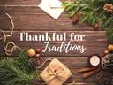 Wooden table with pine branches, pinecones, wrapped gift and candle; text "Thankful for Traditions"