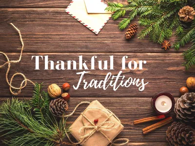 Wooden table with pine branches, pinecones, wrapped gift and candle; text "Thankful for Traditions"