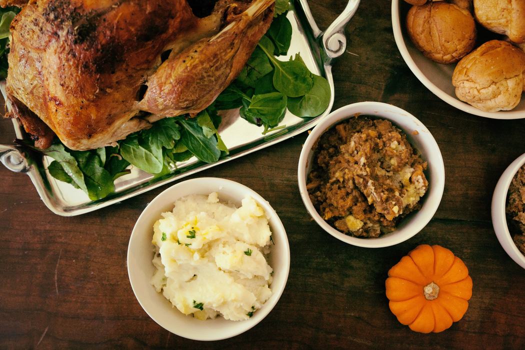 Roasted turkey with bowls of mashed potatoes, stuffing, dinner rolls, and a small pumpkin