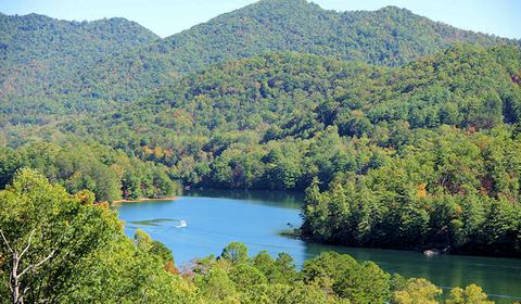 Motorboat creating a wake on a lake surrounded by forested mountains