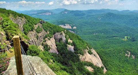 Cliffside overlook with wooden fence railing and forested mountain valley
