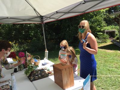 Woman in blue dress and two children wearing masks at an outdoor vendor table