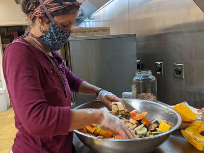 Woman wearing mask and gloves mixing chopped vegetables in a large metal bowl