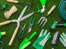 Assorted green gardening tools, gloves, hose and pots laid out on grass.