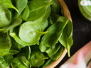 Fresh baby spinach leaves in a wooden bowl on a dark surface with striped cloth.