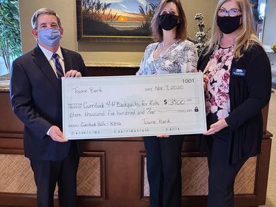 Three masked people holding oversized check from Towne Bank payable to Currituck 4-H Backpacks for Kids $3,500