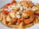 Shrimp and penne pasta with cherry tomatoes and crumbled feta in a bowl