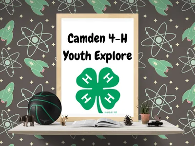 Framed sign reading "Camden 4-H Youth Explore" with green four‑leaf clover logo on a shelf