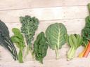 Assorted leafy greens—kale, arugula, spinach, collard, bok choy, Swiss chard—arranged on wood