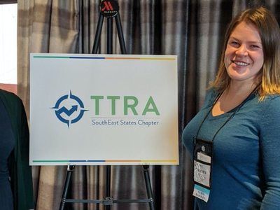 Student, Professor posing in front of TTRA Southeast Chapter sign at conference