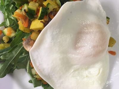 Fried egg atop arugula with sautéed diced zucchini, yellow squash, and carrots on a white plate