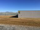 Metal warehouse with colorful logo beside long glass greenhouse under clear blue sky