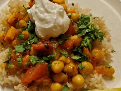 Chickpea and tomato curry over rice topped with yogurt, chopped cilantro and lemon wedge