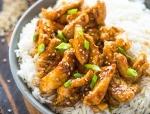 Bowl of rice topped with saucy sesame chicken pieces garnished with chopped green onions