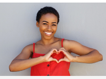 Person in red sleeveless top forming heart shape with hands against gray wall