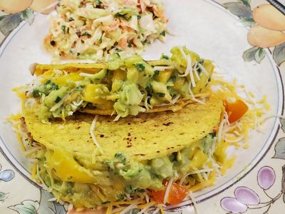 Two corn tacos filled with guacamole, shredded cheese and peppers, served with coleslaw